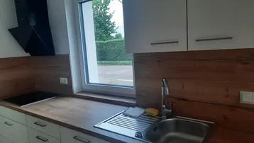 Moderne Einbauküche mit Holz-Arbeitsplatte, Spüle, Induktionskochfeld und Fensterblick ins Grüne.