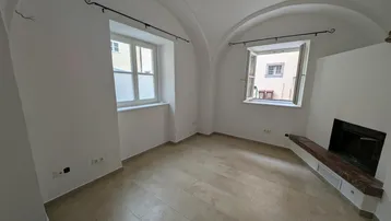 Helles Zimmer mit Gewölbedecke, Fliesenboden und einem gemauerten Kaminbereich.