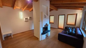 Geräumiges Wohnzimmer mit Holzbalkendecke, Parkettboden und modernem Kamin als Raumteiler.