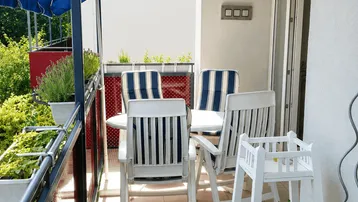 Gemütlicher Balkon mit Fliesenboden, Gartenmöbeln und einem blauen Sonnenschirm.
