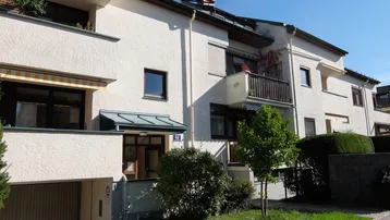 Mehrfamilienhaus mit weißer Fassade, Balkonen und Garagenzufahrt in gepflegtem Zustand.