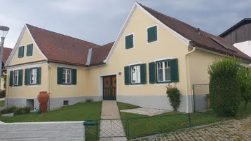 Traditionelles Einfamilienhaus mit gelber Fassade, grünen Fensterläden und Satteldach in ländlicher Umgebung.