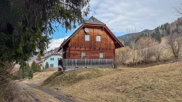 Traditionelles Holzhaus in ländlicher Umgebung mit Blick auf die Berge und einen Feldweg.