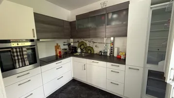 Moderne Küche mit weißen und grauen Schränken, integriertem Backofen und dunklem Fliesenboden.