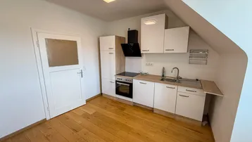 Kleine Einbauküche in einem Dachgeschosszimmer mit Holzfußboden und Dachschräge.