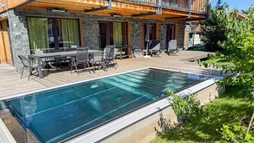 Große Holzterrasse mit Esstisch, Liegestühlen und einem eingelassenen Pool vor der modernen Fassade.