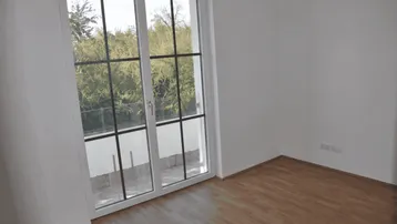Helles Zimmer mit Holzboden und bodentiefen Fenstern, die auf einen französischen Balkon führen.