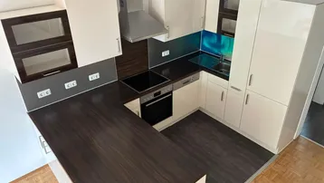 Moderne Einbauküche mit dunkler Arbeitsplatte, hellen Schränken und einem farbigen Spritzschutz.