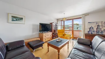 Helles Wohnzimmer mit bequemen Ledersofas, Holzboden und Zugang zum Balkon mit Weitblick.