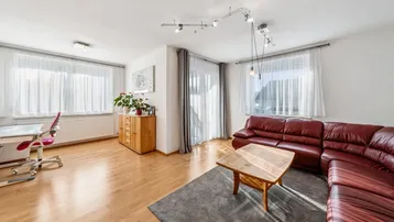 Helles Wohnzimmer mit rotem Ledersofa, Holzboden und einem Arbeitsbereich am Fenster.