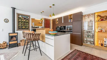 Moderne Küche mit Kochinsel, integrierten Geräten und gemütlichem Kaminofen im offenen Wohnbereich.