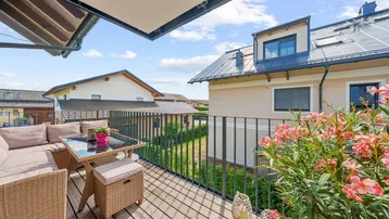 Gemütlicher Balkon mit Holzboden, bequemen Loungemöbeln und Blick auf die umliegenden Häuser.