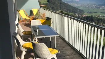Sonniger Balkon mit Holzboden, Sitzgelegenheiten und atemberaubendem Bergblick.