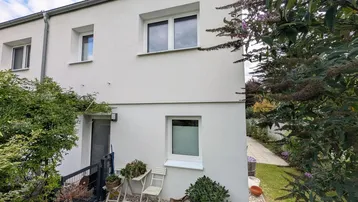Moderne Hausfassade in Weiß mit mehreren Fenstern und seitlichem Gartenbereich.