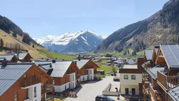 Panoramablick auf ein malerisches Dorf in einem Tal, umgeben von schneebedeckten Bergen und grünen Hängen.