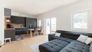 Heller, offener Wohn-Essbereich mit moderner Küche, großem Sofa und Zugang zum Balkon.
