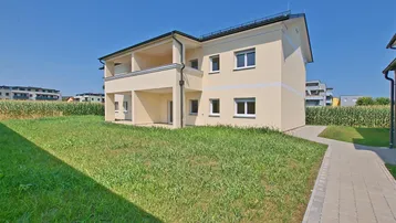 Neubau-Doppelhaushälfte mit heller Fassade und großem Rasenbereich in ländlicher Umgebung.