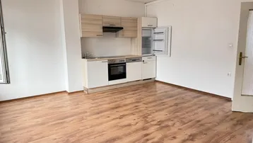 Kleine Einbauküche mit hellen Holzfronten und Laminatboden in einem offenen Raum.