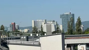 Panoramablick über die Dächer der Stadt mit markanten Hochhäusern und dem Donauturm am Horizont.