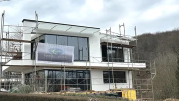 Modernes Neubauhaus im Bau mit Gerüst und einem "Zu Verkaufen"-Banner an der Fassade.