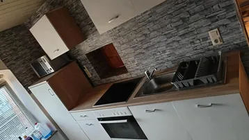 Funktionale Küche mit weißen Fronten, Holzarbeitsplatte und Steinoptik-Rückwand, inklusive Backofen und Kochfeld.