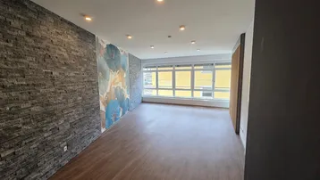 Heller Wohnbereich mit Laminatboden, dekorativer Steinwand und großen Fenstern für viel Tageslicht.