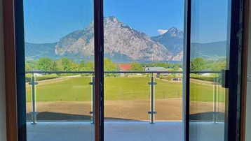 Blick von der Terrasse auf die majestätischen Berge und den See mit grünen Feldern.