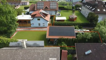 Luftaufnahme eines Wohngebiets mit mehreren Häusern, grünen Gärten und Solaranlagen auf den Dächern.
