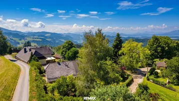 Panoramablick auf ländliche Häuser in einer bergigen Landschaft unter blauem Himmel.