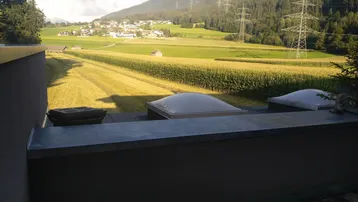 Dachterrasse mit weitem Blick über grüne Felder, ein Dorf und die umliegenden Berge.