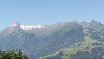 Panoramablick auf majestätische Berge mit schneebedeckten Gipfeln und grünen Tälern unter blauem Himmel.