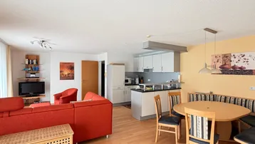 Heller offener Wohn-Essbereich mit integrierter Küche, rotem Sofa und Holzboden.