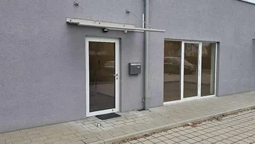 Moderne Gebäudefassade mit Eingangstür, Briefkasten und großen Fenstern, die den Innenraum erhellen.