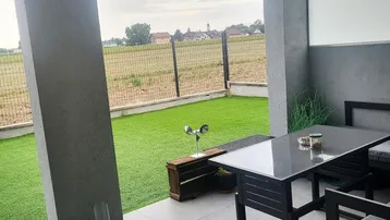Moderne überdachte Terrasse mit Fliesenboden und Blick ins Grüne, ausgestattet mit stilvollen Gartenmöbeln.