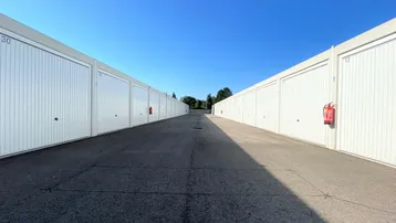 Lange Reihe weißer Garagentore entlang eines asphaltierten Weges unter blauem Himmel.