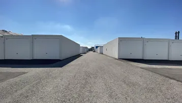 Reihe von weißen Garagenboxen unter strahlend blauem Himmel mit Schotterweg im Vordergrund.