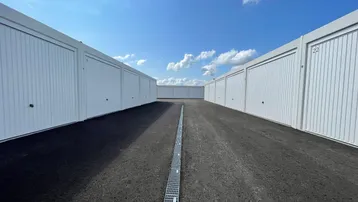 Reihen von modernen Garagenboxen unter blauem Himmel mit asphaltiertem Zufahrtsweg.