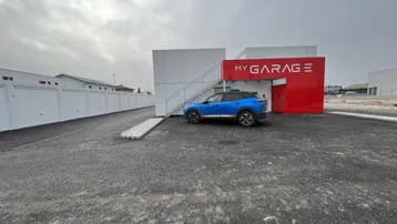 Außenansicht einer modernen Garagenanlage mit Parkplätzen und einem blauen Auto davor.