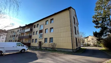 Mehrfamilienhaus mit gelber Fassade und Balkonen unter blauem Himmel an einem sonnigen Tag.