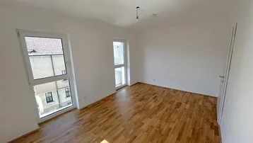 Helles Schlafzimmer mit Eichenparkett und zwei Fenstern, eines davon als französischer Balkon.