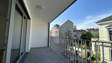 Heller Balkon mit Fliesenboden und Blick auf die umliegenden Gebäude und die Straße.