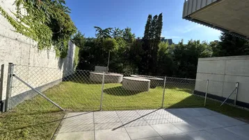 Außenbereich mit Rasenfläche, gepflasterter Terrasse und dekorativen Pflanzgefäßen unter blauem Himmel.
