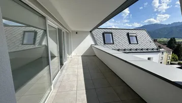 Geräumiger Balkon mit Fliesenboden, weißer Brüstung und weitem Blick auf die Berge und Dächer.