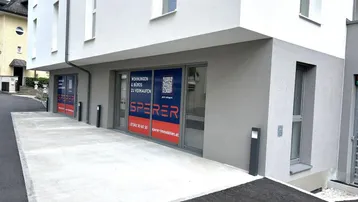 Modernes Gebäude mit hellgrauer Fassade und großen Schaufenstern für Gewerbeflächen im Erdgeschoss.
