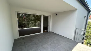 Geräumiger Balkon mit modernen Fliesen, Glasfront und Blick ins Grüne.