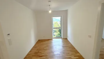 Helles Zimmer mit Holzboden und Blick ins Grüne, ideal als Schlaf- oder Wohnbereich.