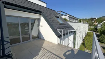 Heller Balkon mit Fliesenboden und Blick auf die umliegende Bebauung und Hügel.