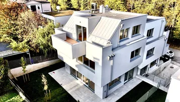 Moderne Architektur eines Mehrfamilienhauses mit Flachdach und Balkonen, umgeben von Bäumen.