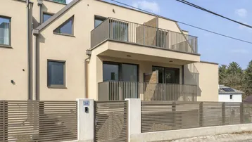 Modernes Mehrfamilienhaus mit beigefarbener Fassade, Balkonen und einem eleganten Zaun an der Straße.