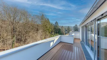 Geräumige Terrasse mit modernem Holzboden und weitem Blick auf die umliegende Natur und bewaldete Hügel unter blauem Himmel.